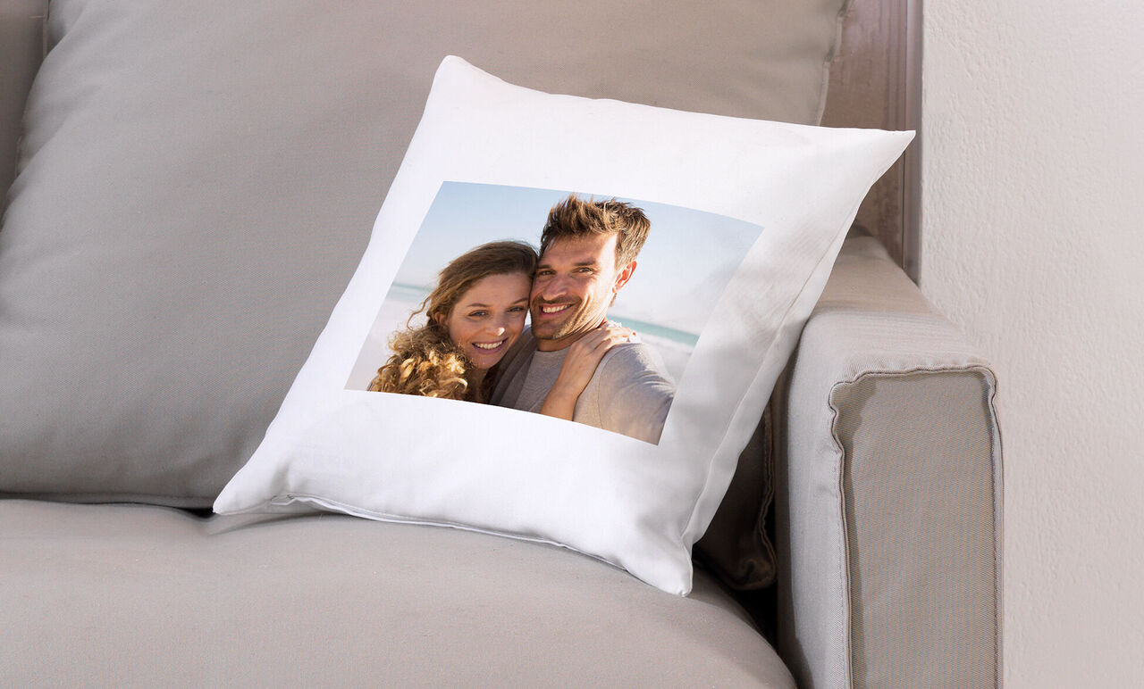 Pude med foto af to personer på stranden, solskin på en hyggelig sofa.