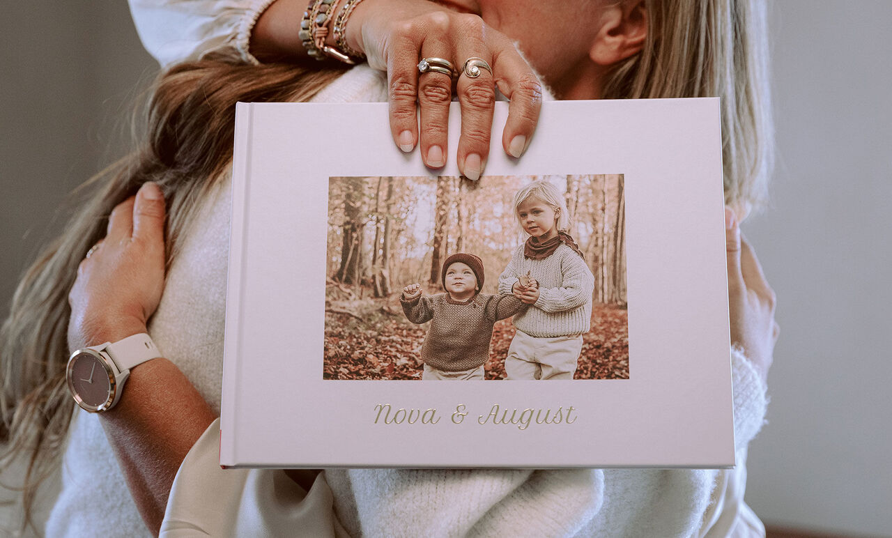 En person holder en fotobog med et billede af to børn i en skov.