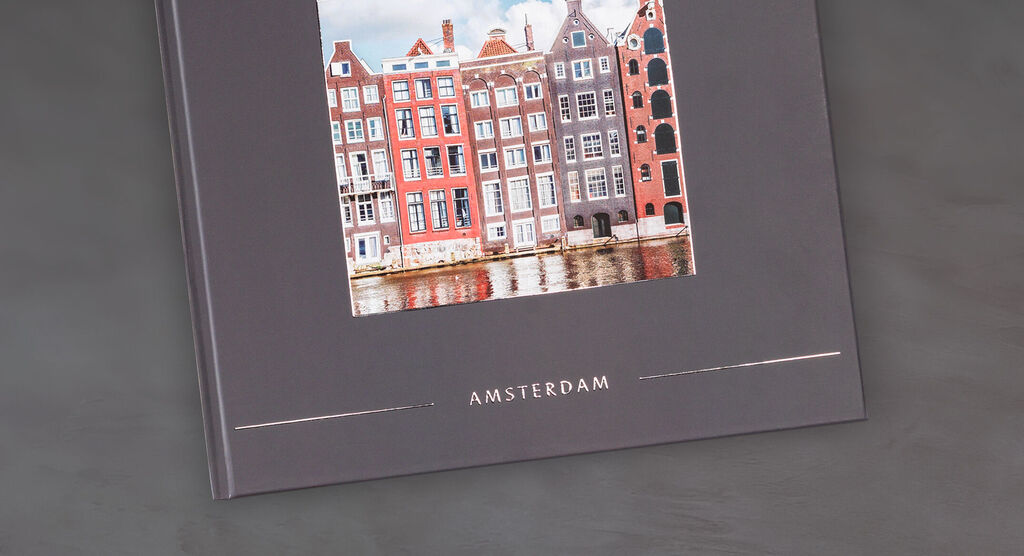 En CEWE FOTOBOG med et smukt foto af farverige huse i Amsterdam på en elegant, grå baggrund.