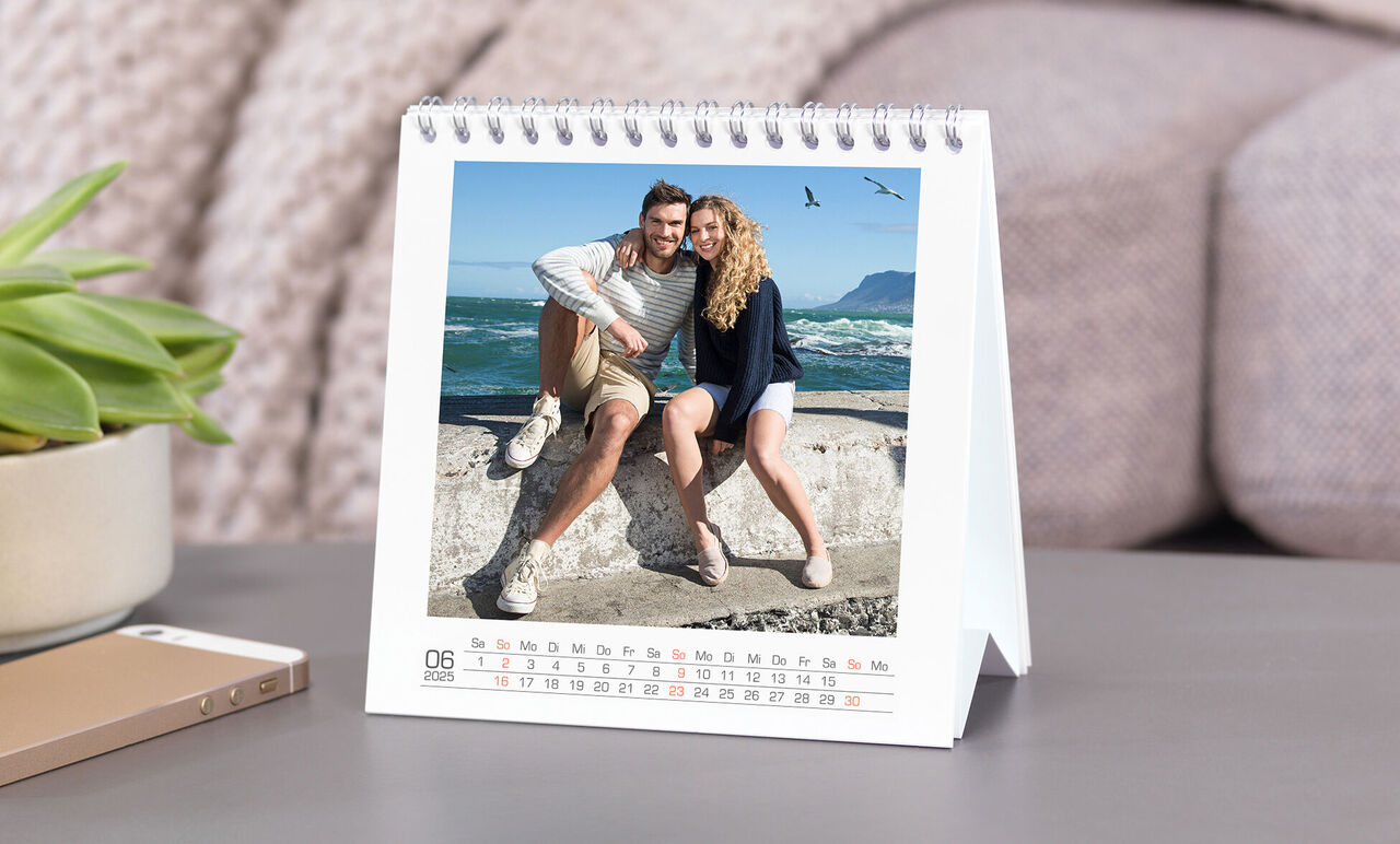 En personlig fotokalender med et lykkeligt par på stranden. De smiler og poserer sammen, bølgerne ses bag dem.