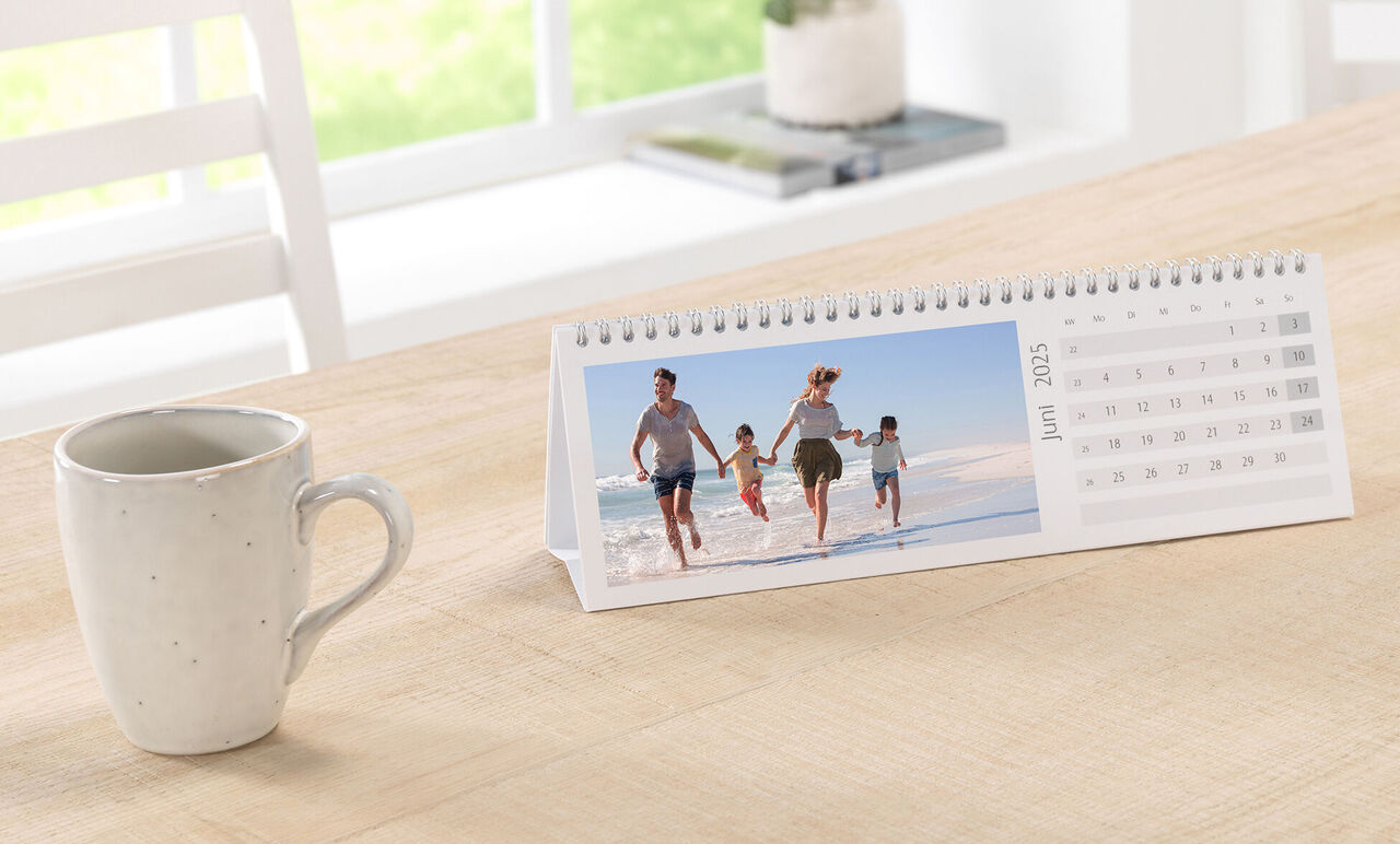 Familien går på stranden og nyder sommeren. En CEWE fotokalender viser juni måned.