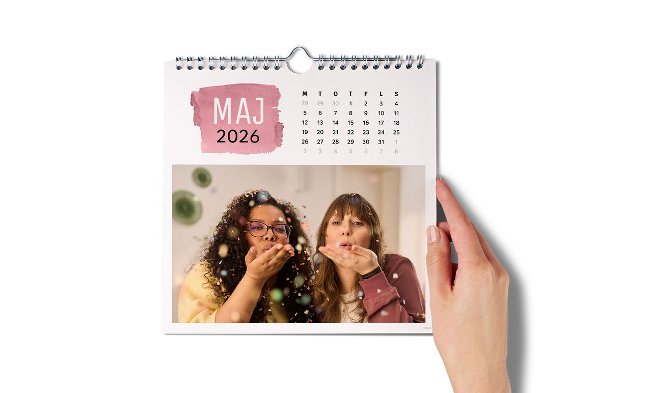 En hånd holder en vægkalender med et glædeligt billede af maj 2025