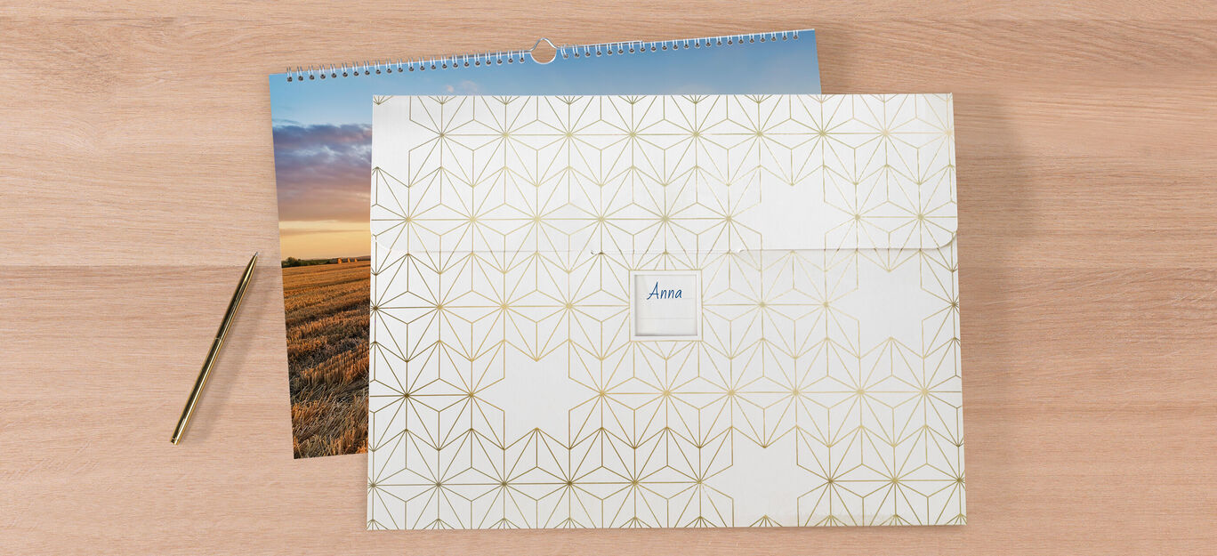 En dekorativ kuvert med gyldne geometriske mønstre, ved siden af en kalender med landskabsbillede.
