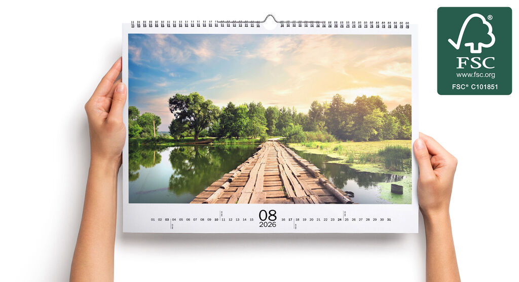 En person holder en vægkalender med smukt landskab for august 2022.