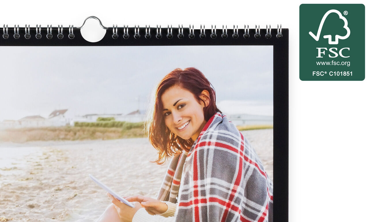 En person nyder deres CEWE fotokalender, mens de slapper af på stranden.