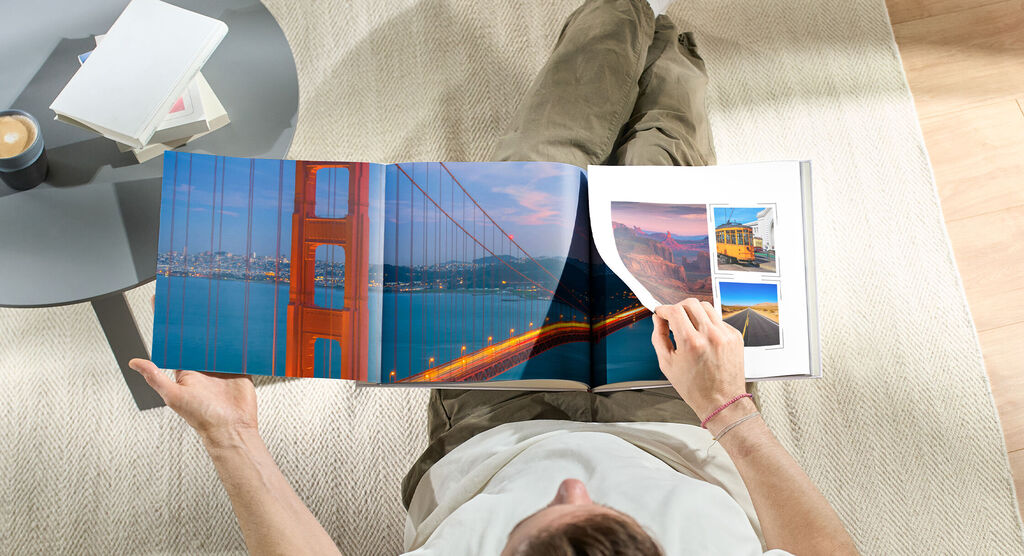 En person bladrer gennem en CEWE Fotobog med billeder af Golden Gate Bridge og rejseminder.