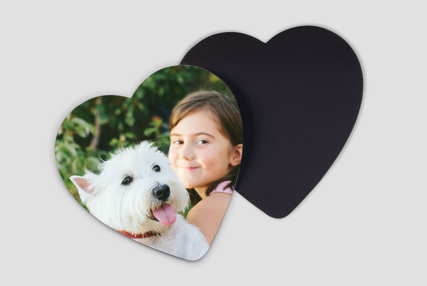 En hund med hvid pels og lyserød tunge poserer foran en pige med mørk baggrund på et hjerteformet kort.