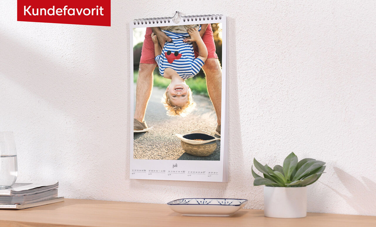 En ophængt vægkalender viser et glad barn på hovedet, med et smil og lyse strømper.