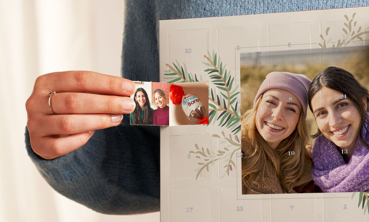 Hånd holder et børnefoto og en chokolade foran et adventsmotiv.