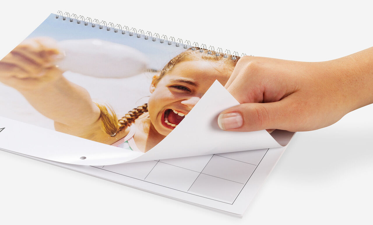 En hånd bladrer gennem en fotokalender, glade ferie billeder synlige.