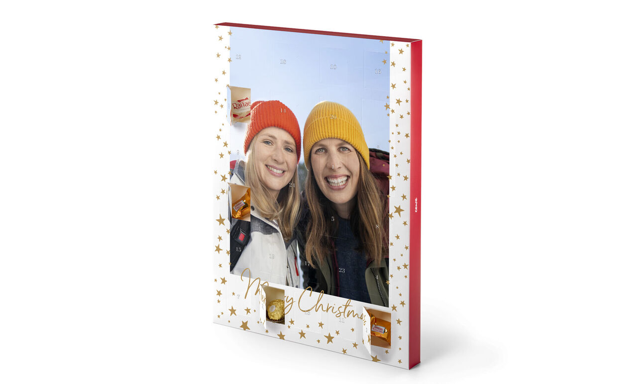 CEWE fotobog med juledesign, to personer holder den. Omslaget har gyldne stjerner og teksten "Merry Christmas".