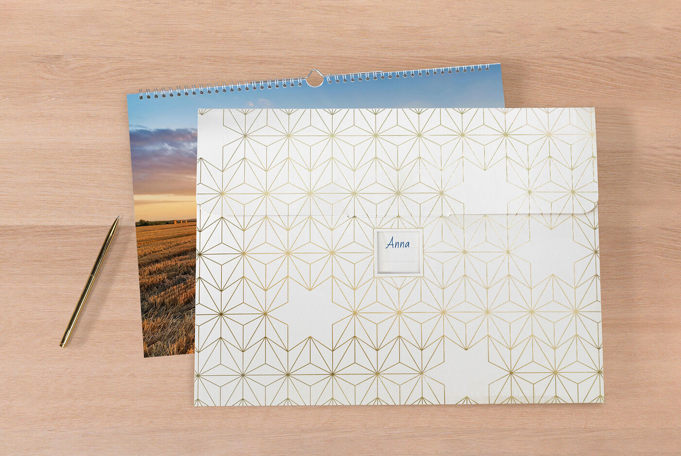 En kærligt designet CEWE fotokalender på et træbord med en dekortaske 'Anna' og en gylden pen.