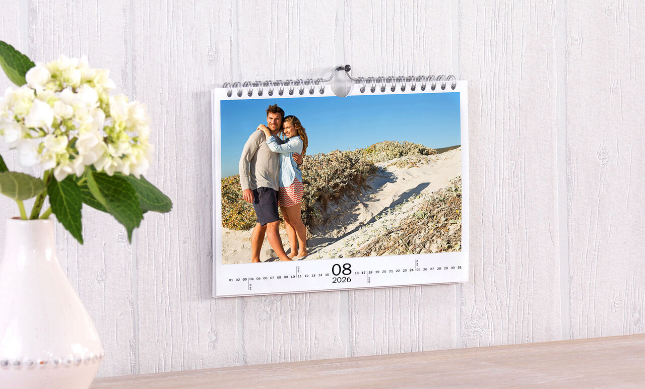 En smuk vægkalender med et billede af et par på stranden. Kalenderen viser august 2023.