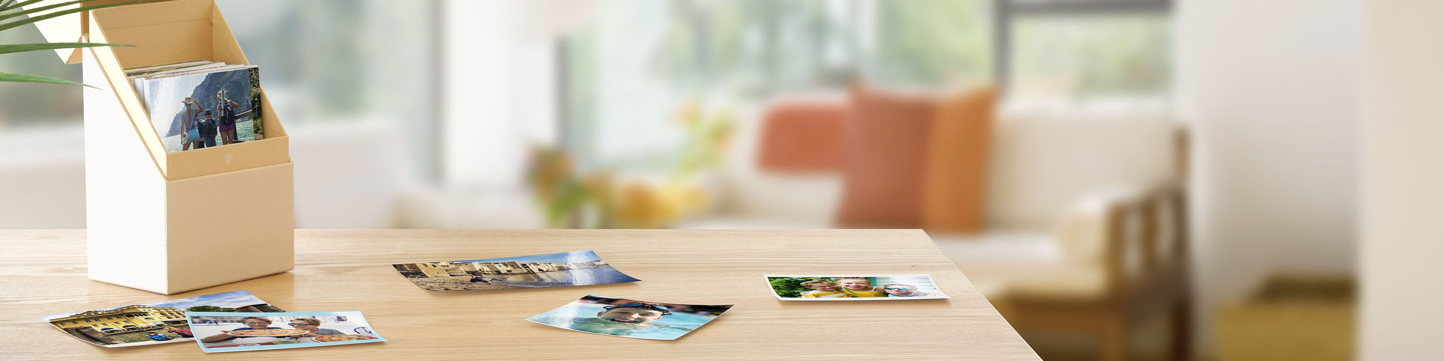En træholder med fotos og postkort på et bord. Baggrunden viser en stue med sofa og planter.