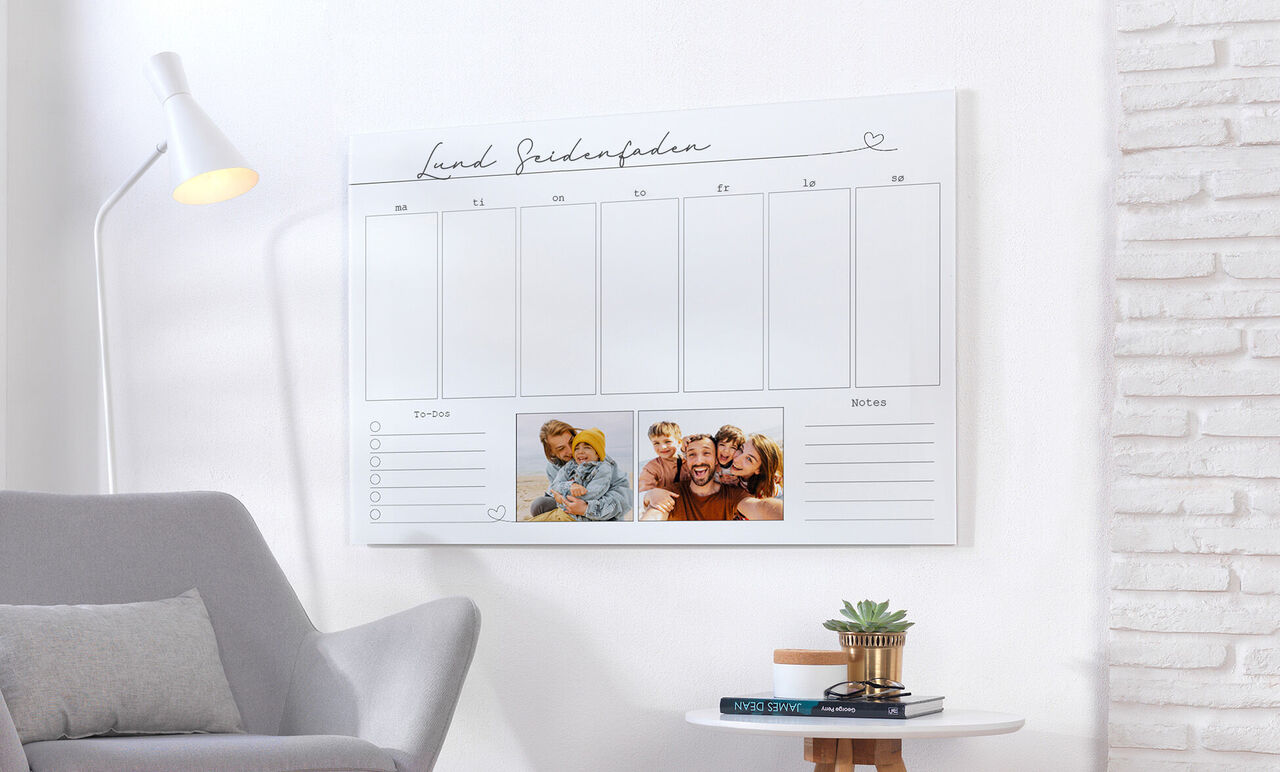 En KEWE fotokalender på en væg i et hyggeligt rum med en grå sofa og en lampe