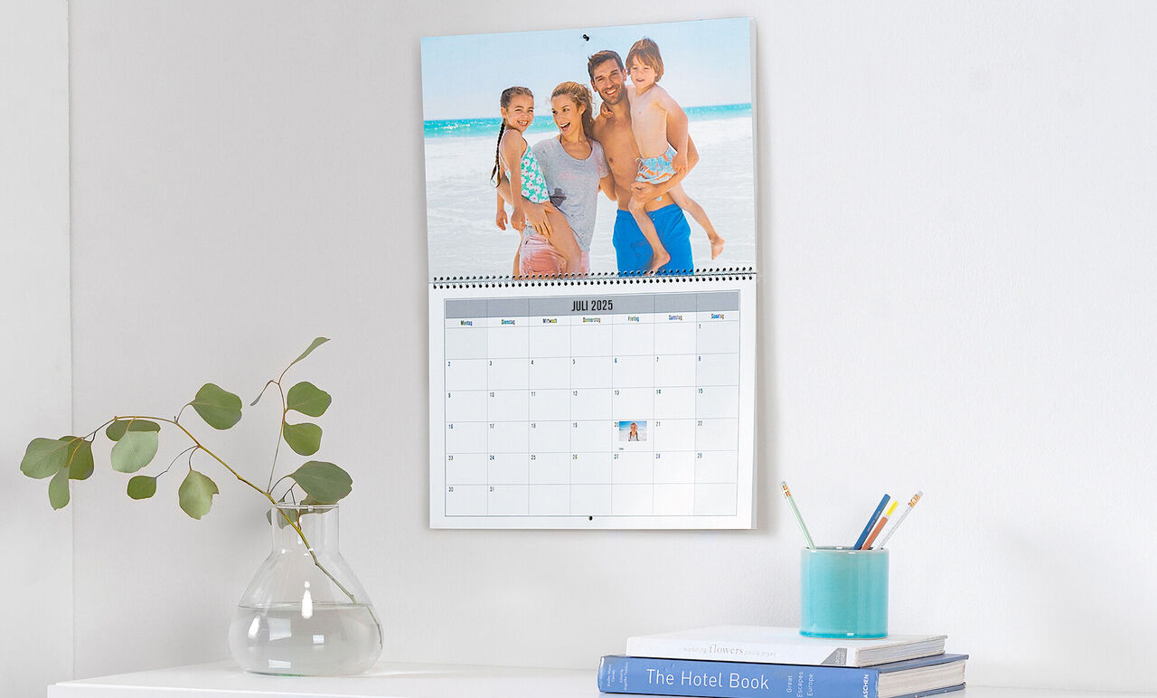Familie poserer glad foran en kalender på væggen med feriemotiver.