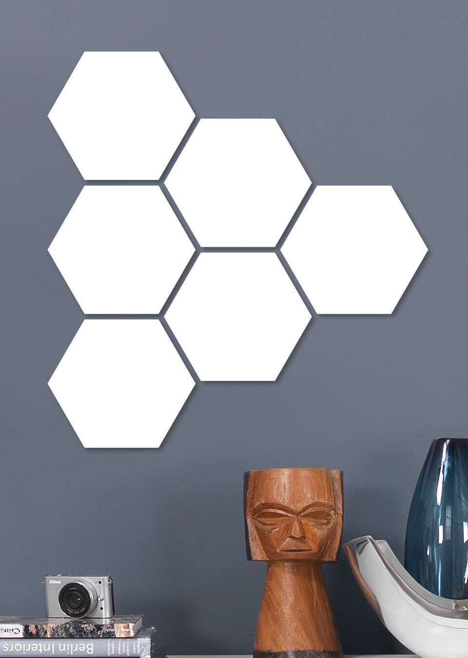 Seks hvide sekskantede former på en grå væg, ved siden af en moderne lampe og kamera.