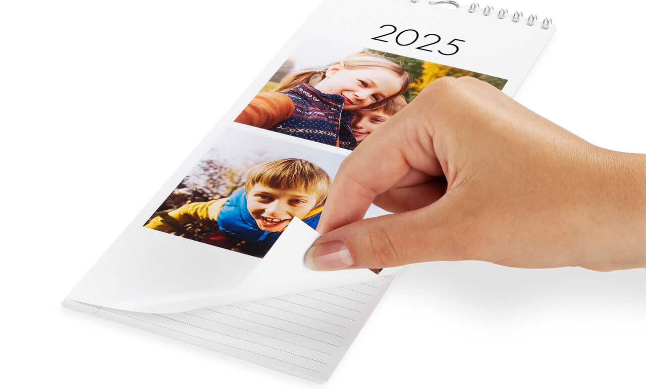 En hånd bladrer gennem en CEWE fotokalender for 2025 med billeder af lykkelige øjeblikke.