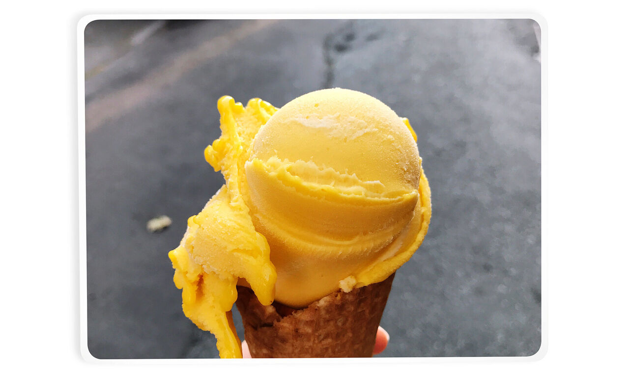 Isbold af gul sorbet på en vaffel i hånden.
