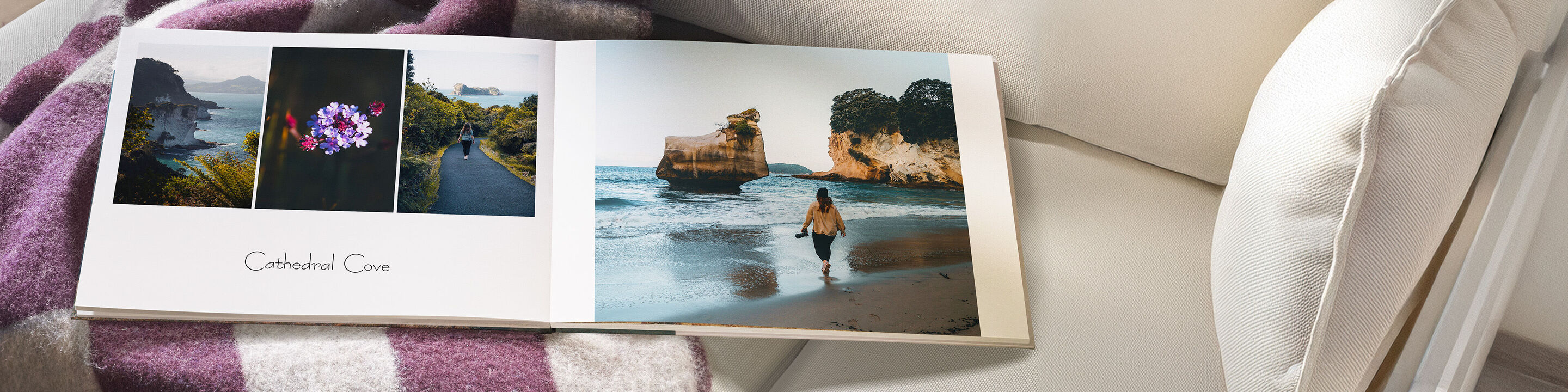 En åben fotobog ligger på en hvid sofa. Den viser en strandnær scene med en person ved vandet og to andre billeder. Perfekt til minder.