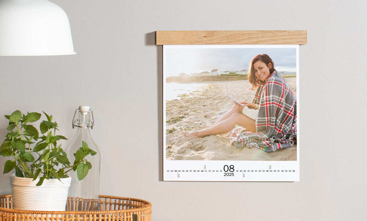 Person sidder afslappet ved stranden med en bog i CEWE fotokalenderen, der viser august 2025.