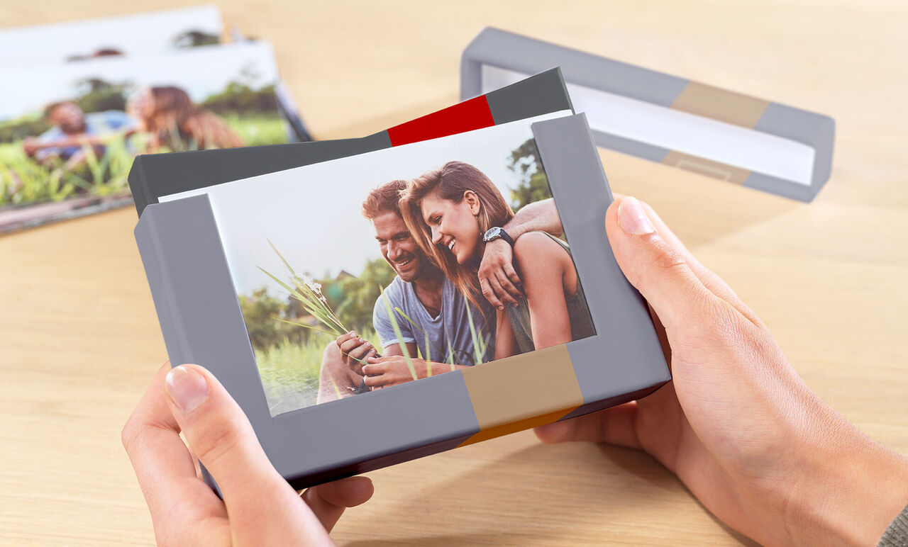 En person holder en fotobog med et smukt billede i hænderne. I baggrunden ses flere fotobøger, der deler følelsesmæssige øjeblikke.