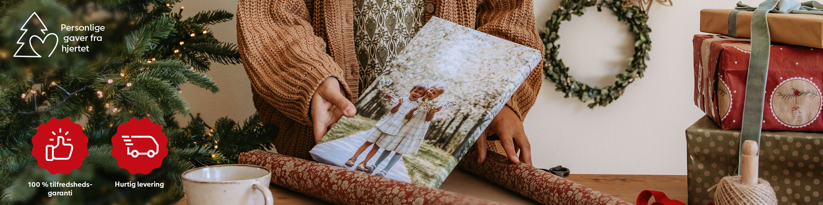 En person holder en fotoplakat med et par udendørs, omgivet af gaver og gavepapir.
