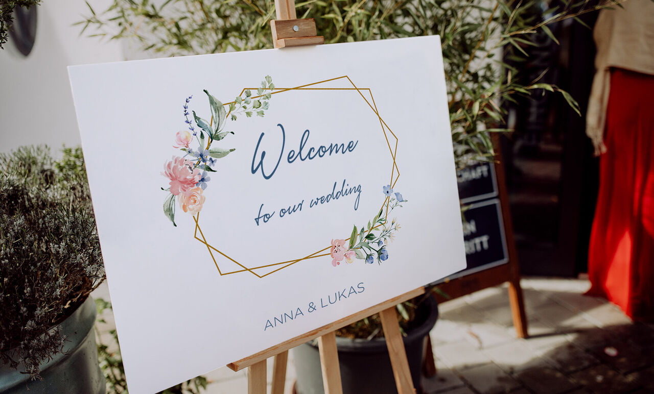 Et dekorativt velkomstskilt til et bryllup med florale elementer og navnene Anna og Lukas.