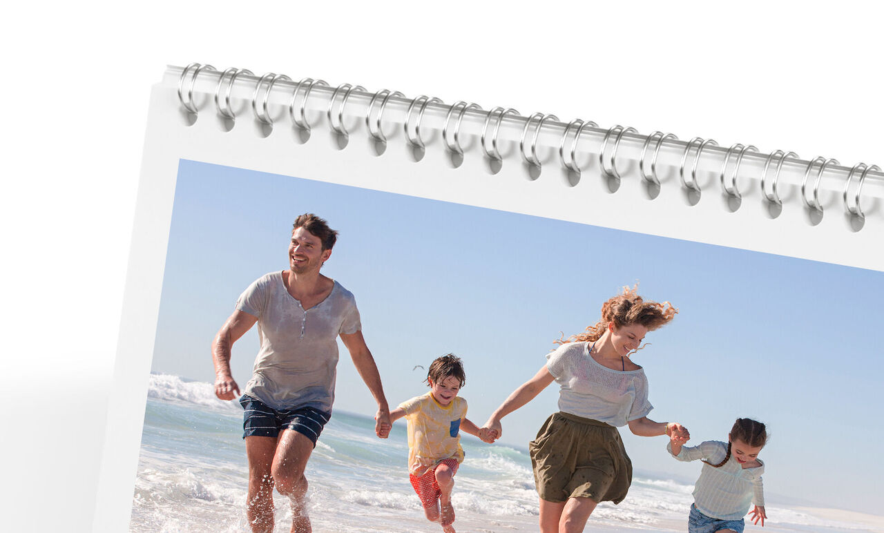 Familien går glade langs stranden og nyder solen. CEWE fotokalender.