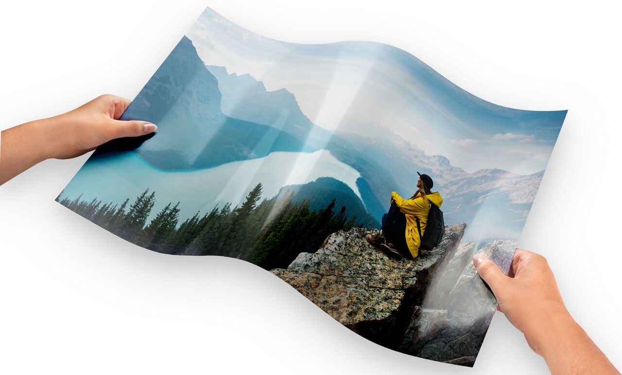 Person i gul jakke sidder på klippe og ser på en sø og bjerge