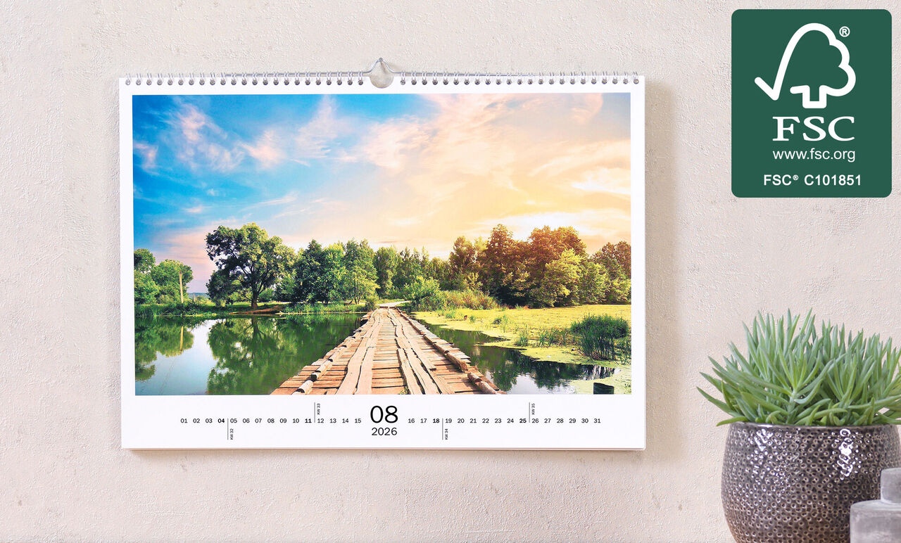 Hængende fotokalender viser et malerisk landskab med en træbro over et stille vand omgivet af frodig grøn.