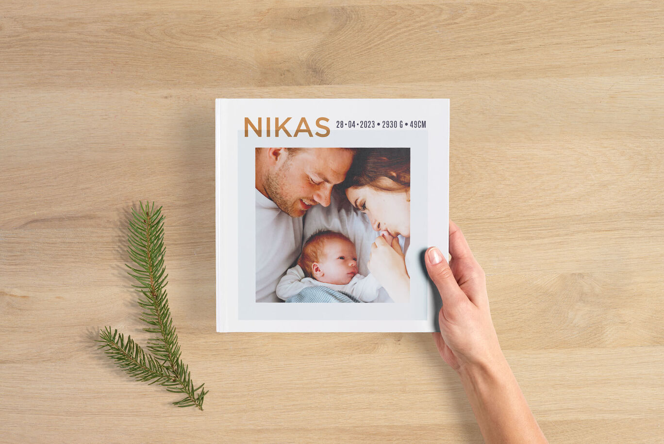 En hånd holder en CEWE fotobog med et babyfoto og et behageligt design.