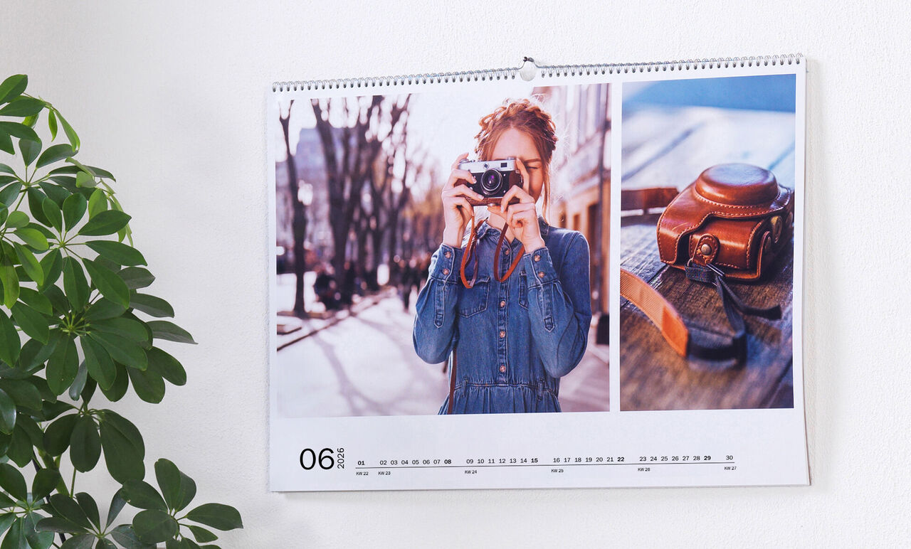 En vægkalender med billede af en person der fotograferer og et gammelt kamera på et bord.