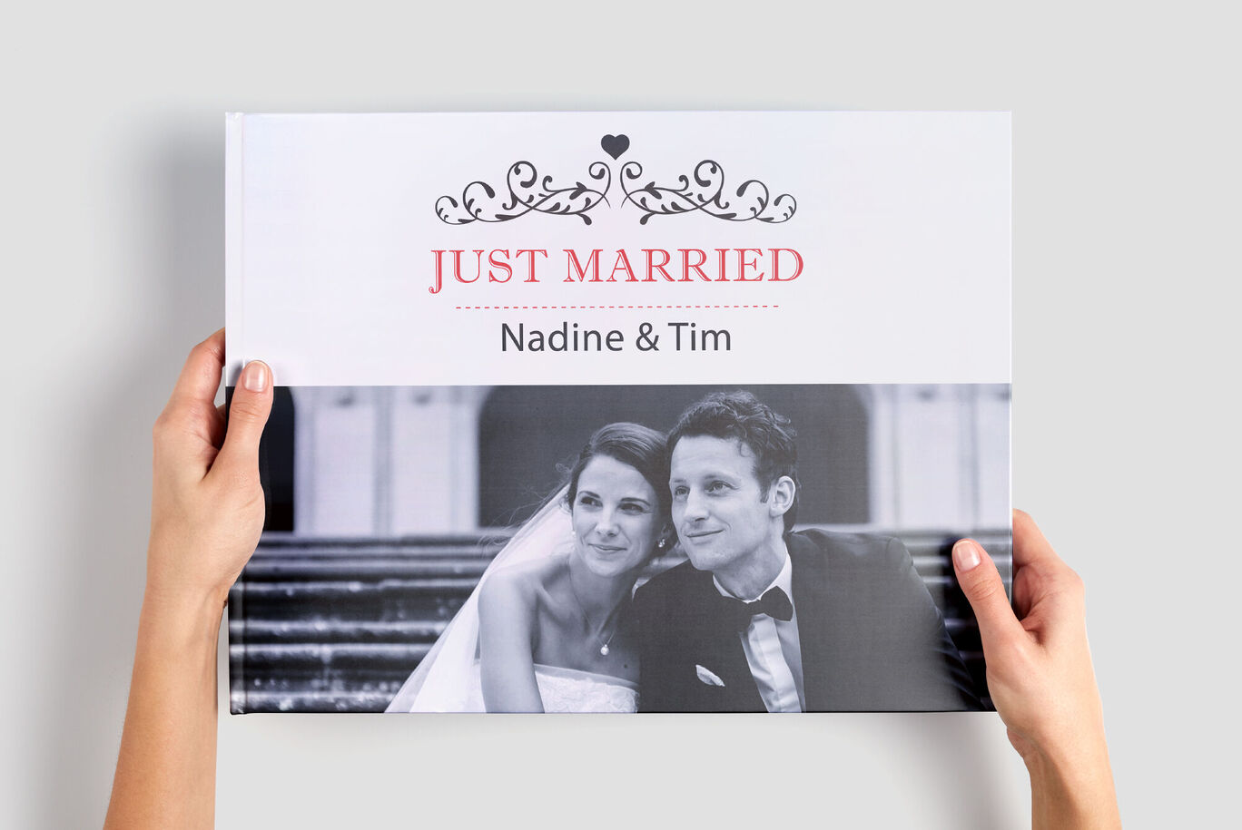 Hænder holder en CEWE FOTO BOG med titlen 'Just Married' og navnene 'Nadine & Tim'.