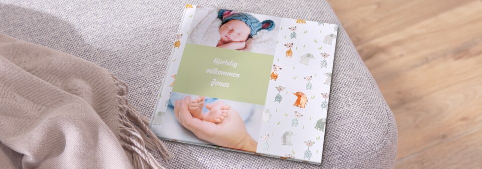 En CEWE fotobog med et sødt babybillede på forsiden, omgivet af farverige dyremotiver.