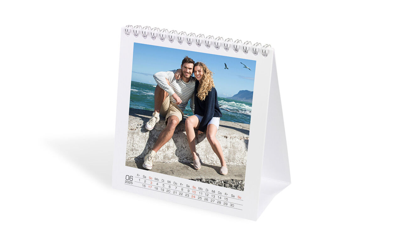 To venlige personer poserer glade foran en kystlandskab i en bordkalender.