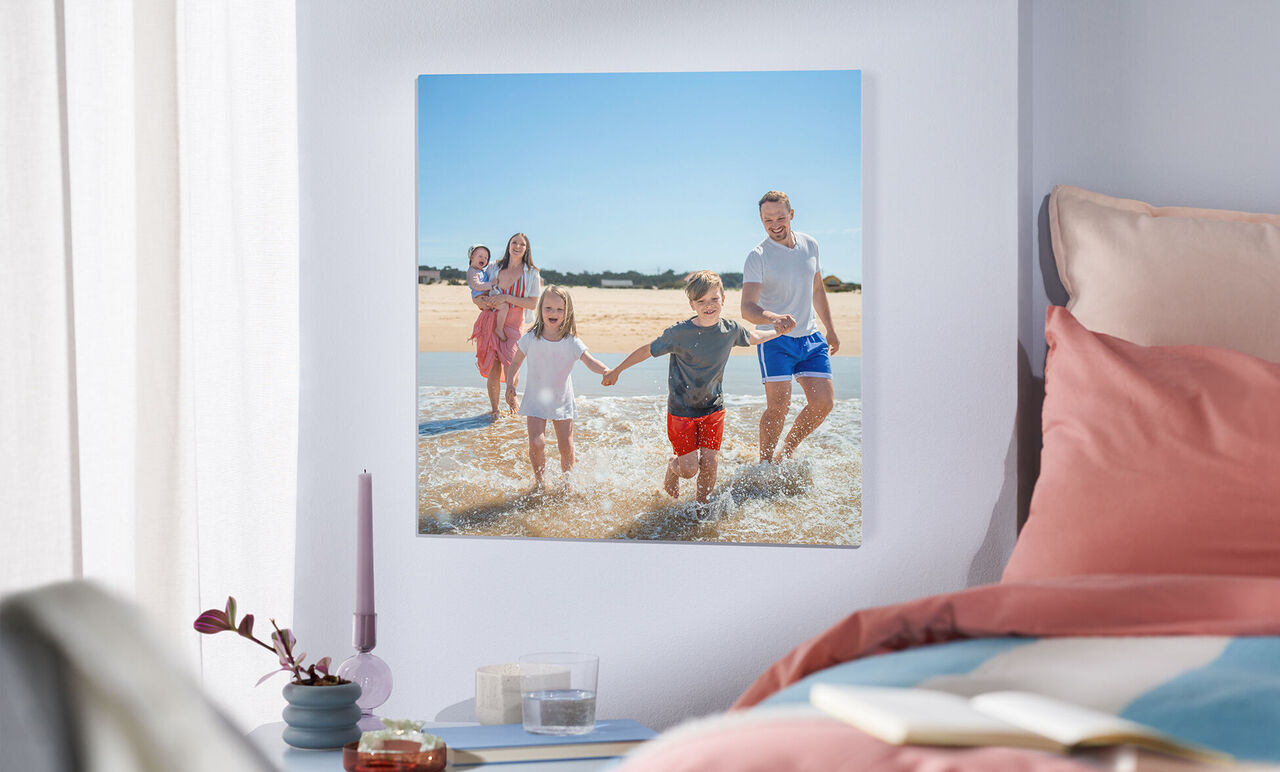 En glad familie leger i vandet på stranden. To voksne og to børn holder hænder. Sollys stråler ned på dem.