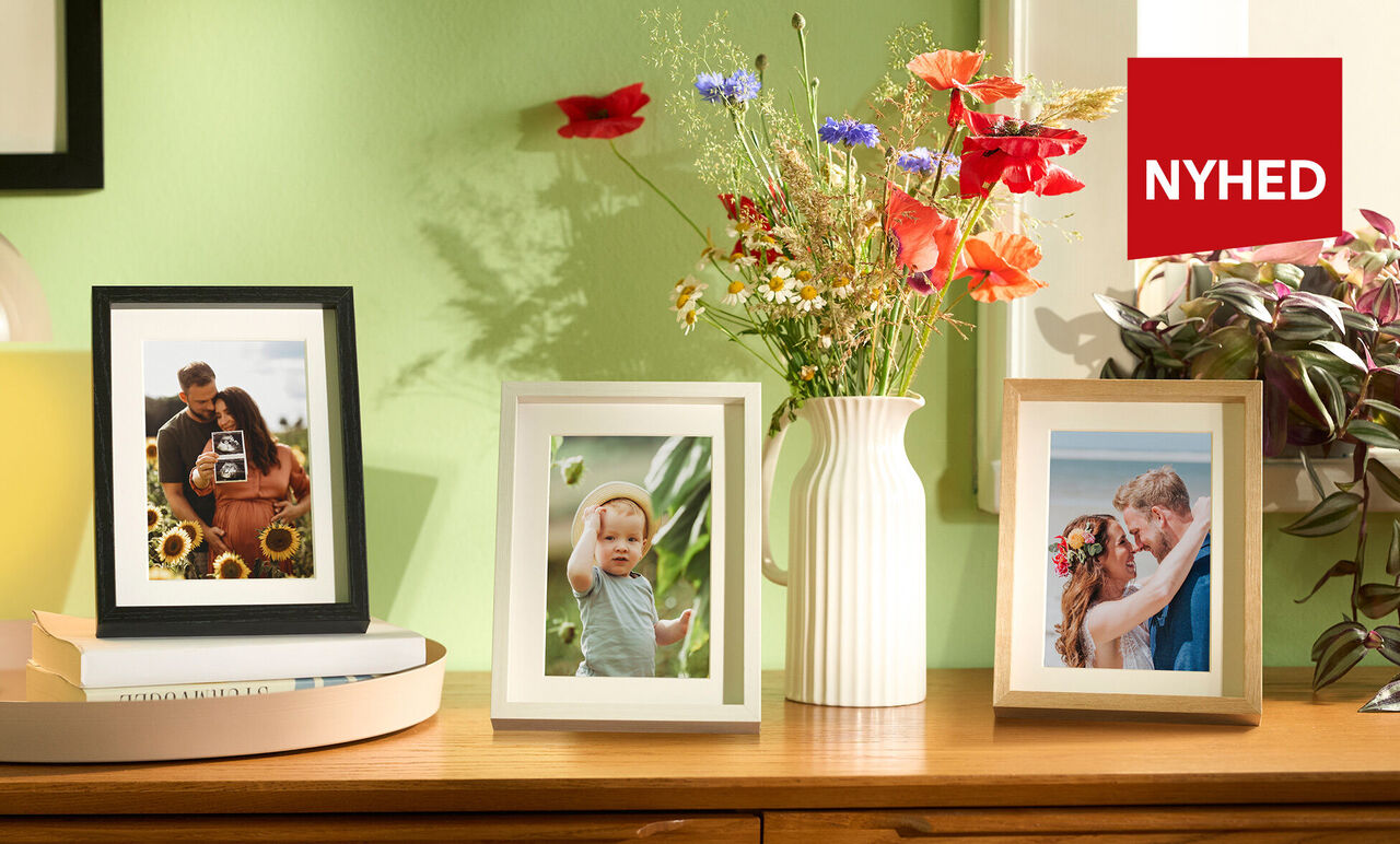 Tre indrammede fotos på et træbord, omgivet af farverige blomster i en vase.