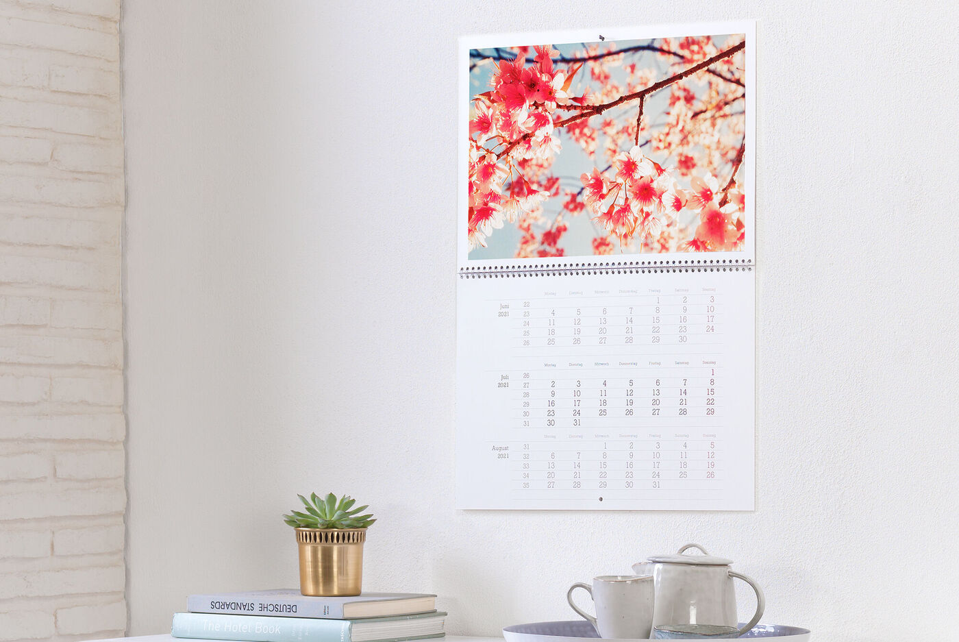En CEWE fotokalender med kirsebærblomster i baggrunden, hængende på en hvid væg.