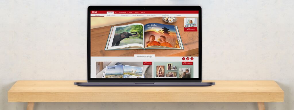 Bærbar computer viser CEWE FOTOBUCH med farverige billeder på skærmen.