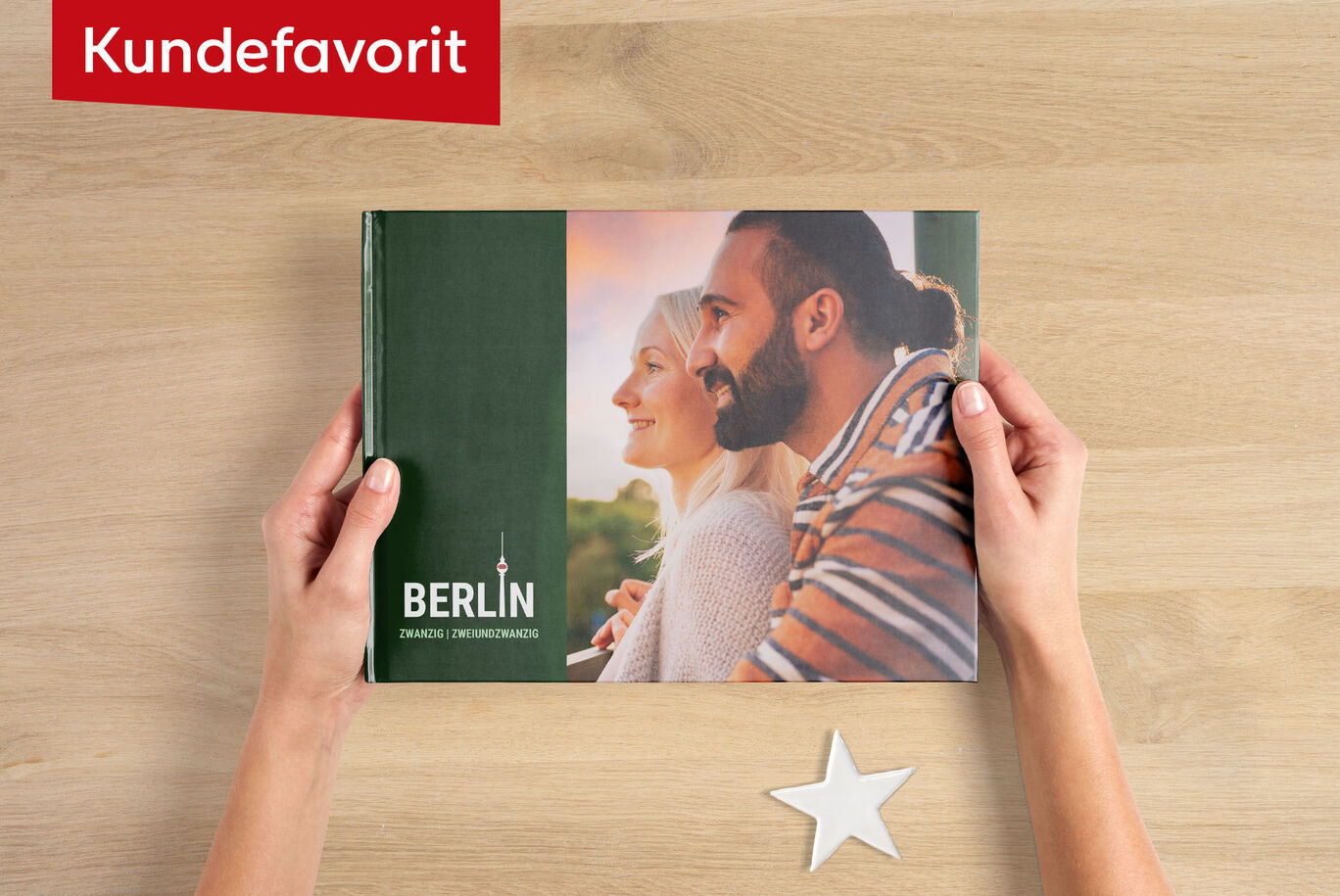 En person holder en CEWE FOTOBOG med titlen 'BERLIN' i hænderne på en træoverflade.