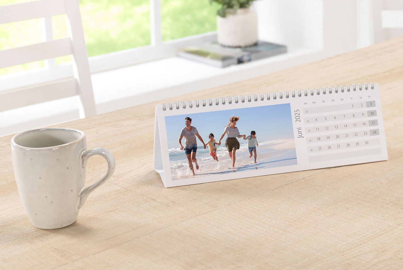 En CEWE fotokalender på et bord viser en glad familie, der går en tur på stranden