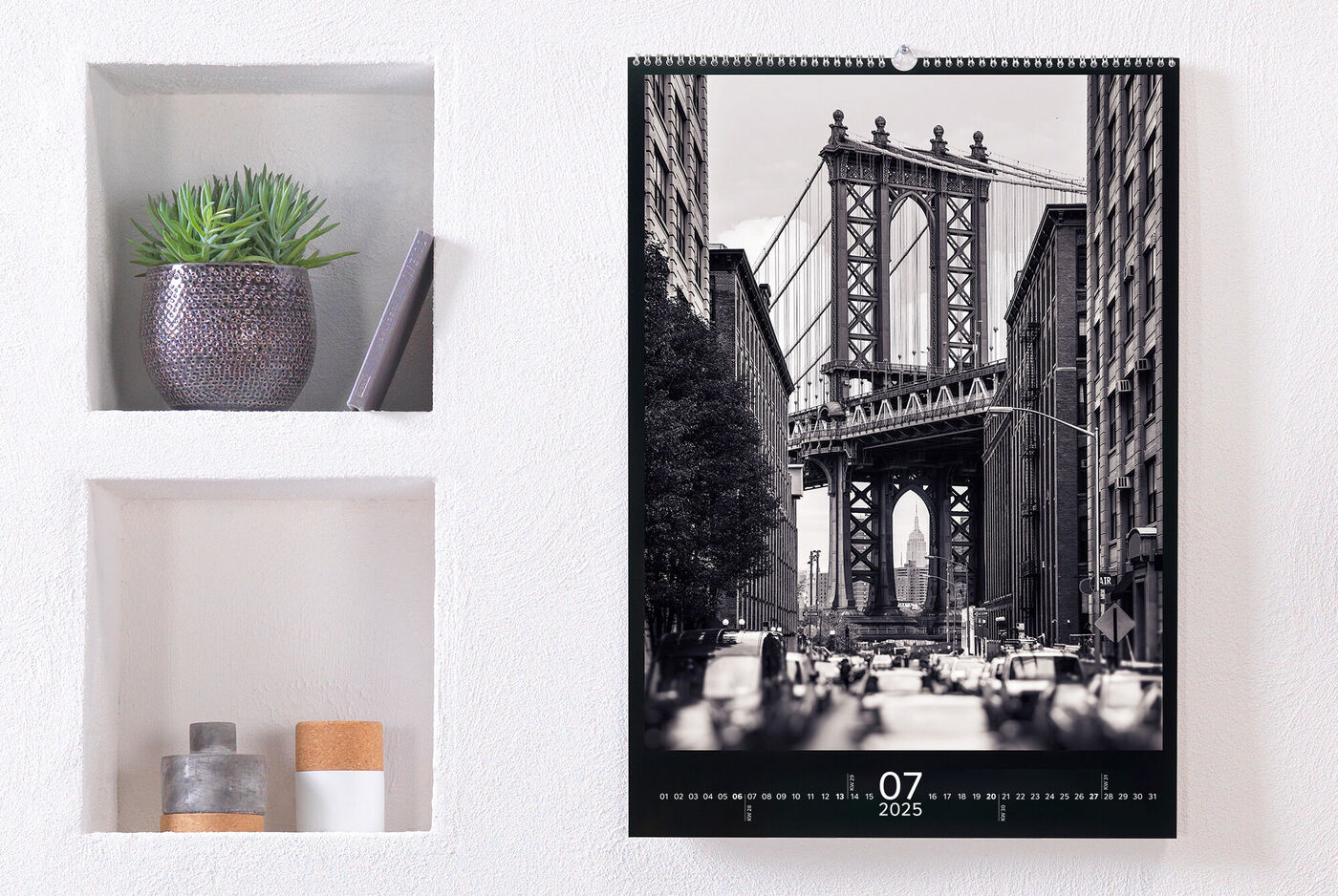 En stilfuld fotokalender hænger på en væg. Juli 2025 med billedet af Brooklyn Bridge i sort-hvid.