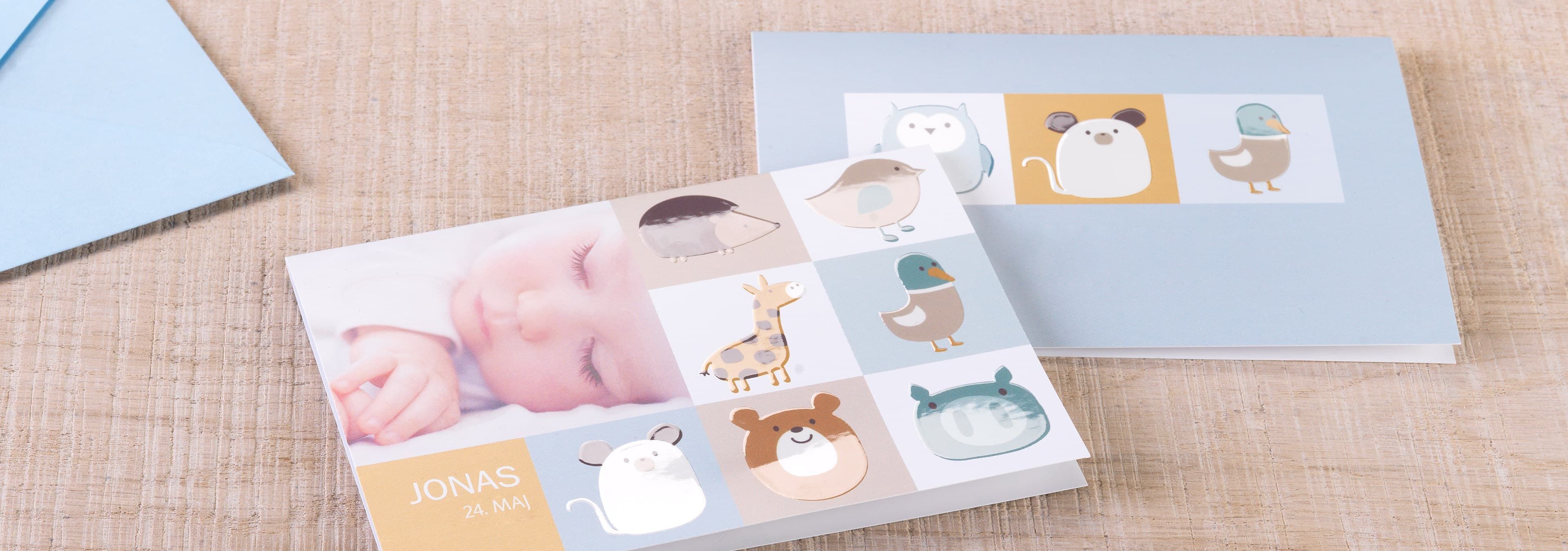 To smukt designede CEWE fotoalbum med dyremotiver og et babyfoto på forsiden står på en naturlig, lys baggrund. Den venstre bog har en personlig dedikation.