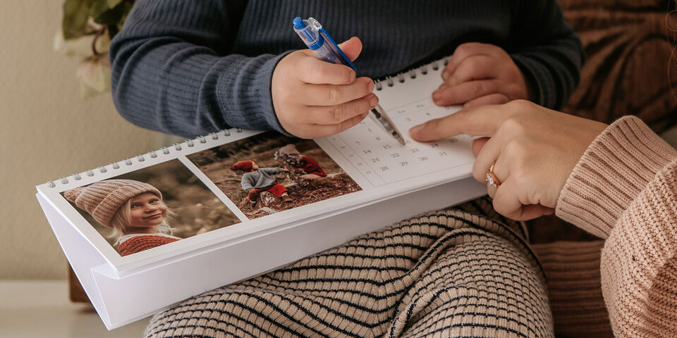 Et barn og en voksen fokuserer på en kalender, hvor de skriver